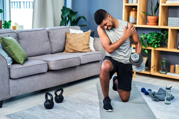 Shot of a young man suffering from fractured shoulder while exercising at home