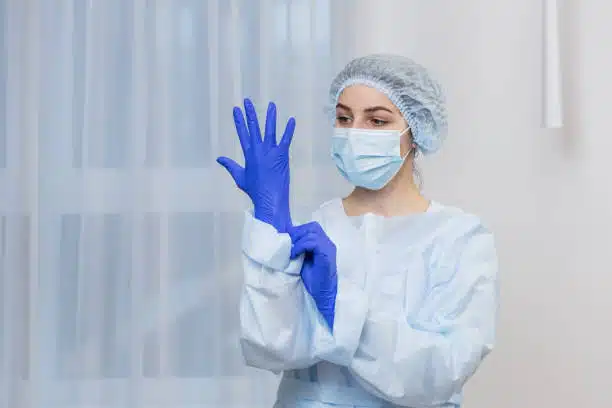 Young female surgeon prepares for surgery, wears blue surgical gloves and white coat