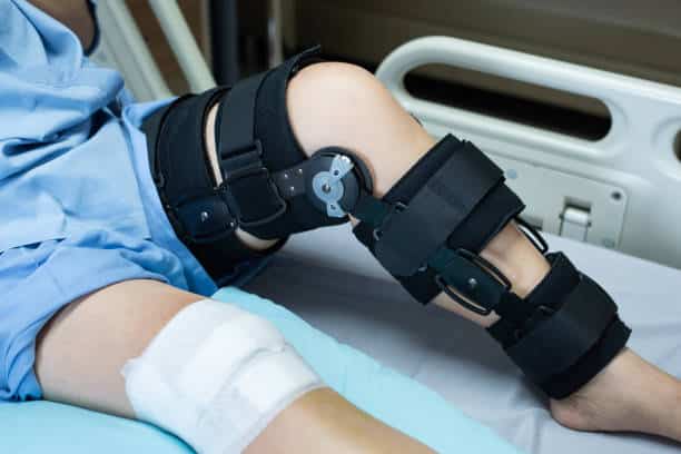 Patient with knee brace support lying on a hospital bed after a knee surgery at the surgery center.