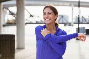 Woman taking a break from running to stretch her arms and shoulders.