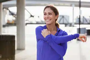 Woman taking a break from running to stretch her arms and shoulders.